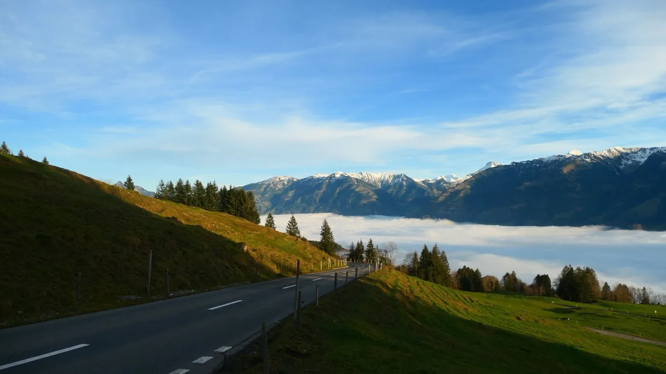 Eine Bergstrasse führt über einem Wolkenmeer in den Schweizer Alpen